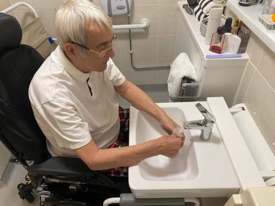 Gentleman in a powerchair uses Ropox QuickWash basin to wash hands.